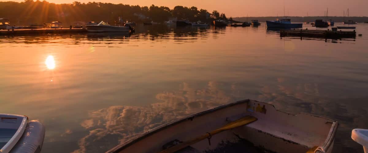 A calm harbor at sunset with boats docked, a wooden pier, and a clear sky.