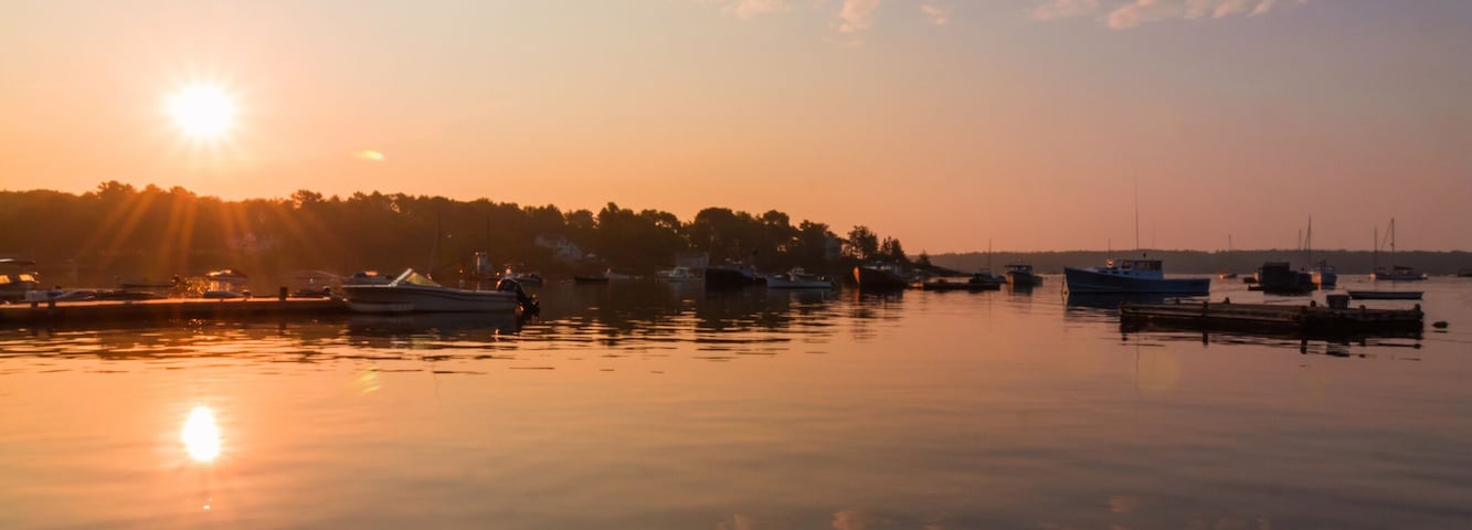 A calm harbor at sunset with boats docked, a wooden pier, and a clear sky.