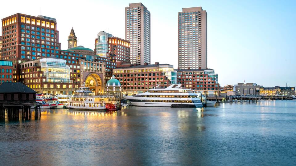 A waterfront cityscape with historic buildings, a prominent clock tower, and a modern high-rise.