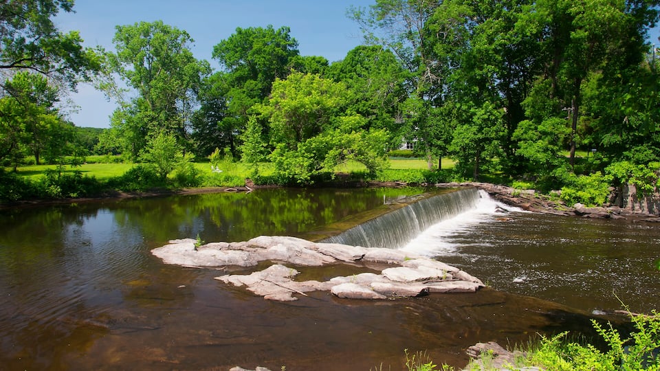 A waterfall cascading over rocks into a clear river surrounded by lush greenery and trees.