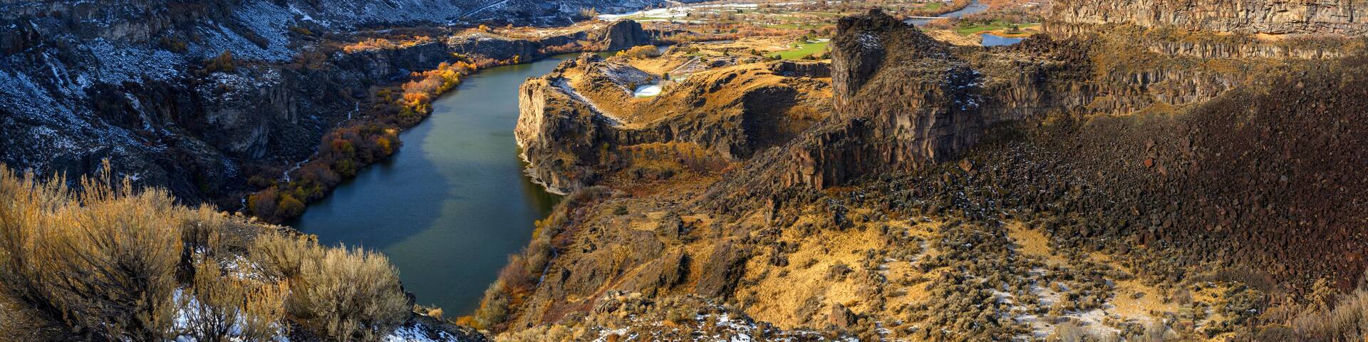 A canyon with a river, rocky cliffs, and sparse vegetation.