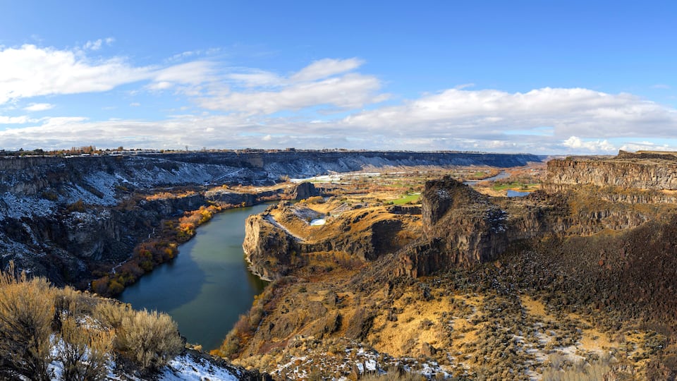 A canyon with a river, rocky cliffs, and sparse vegetation.