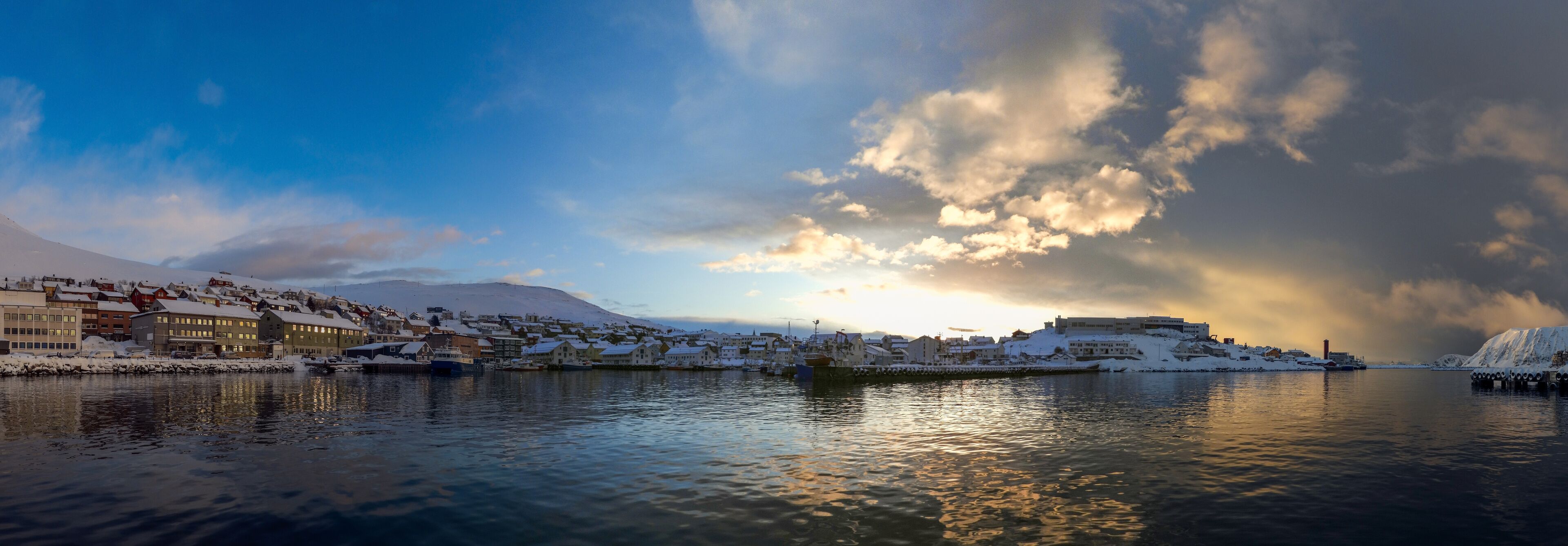 A snowy coastal town with buildings and a mountain in the background.