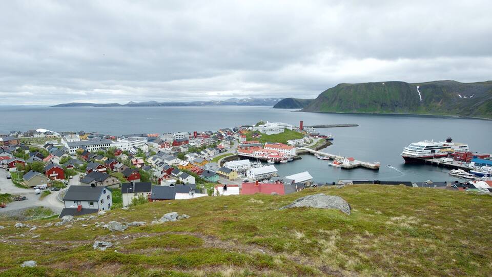 A coastal town with colorful houses, a harbor with boats, and mountains in the background.