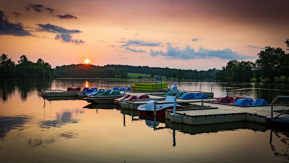 A lakeside dock with colorful boats and a sunset in the background.