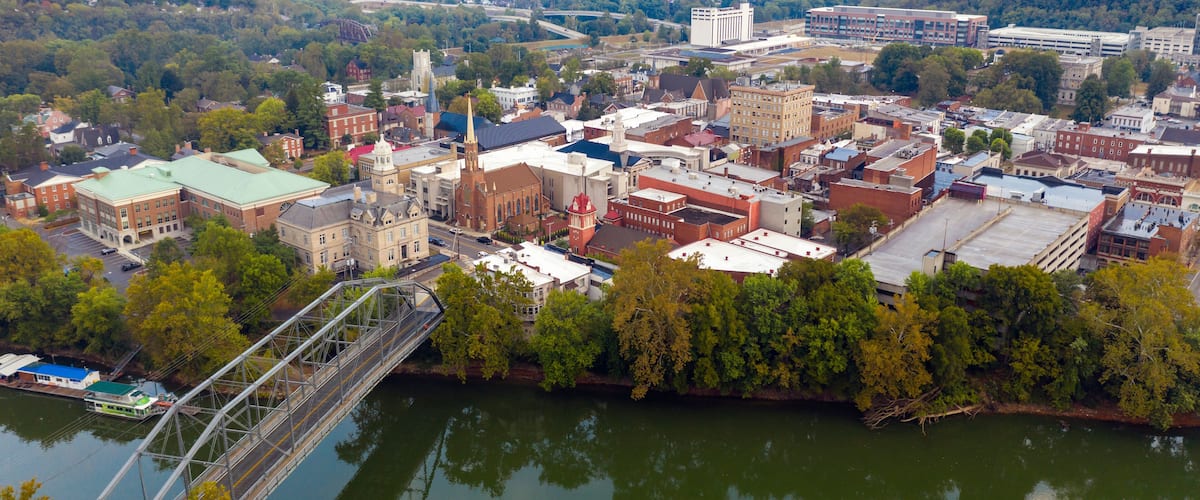 A riverside town with historic buildings, a bridge, and a distant bridge over the river.