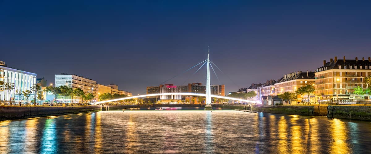 A nighttime cityscape with a prominent illuminated bridge over a river, reflecting city lights.