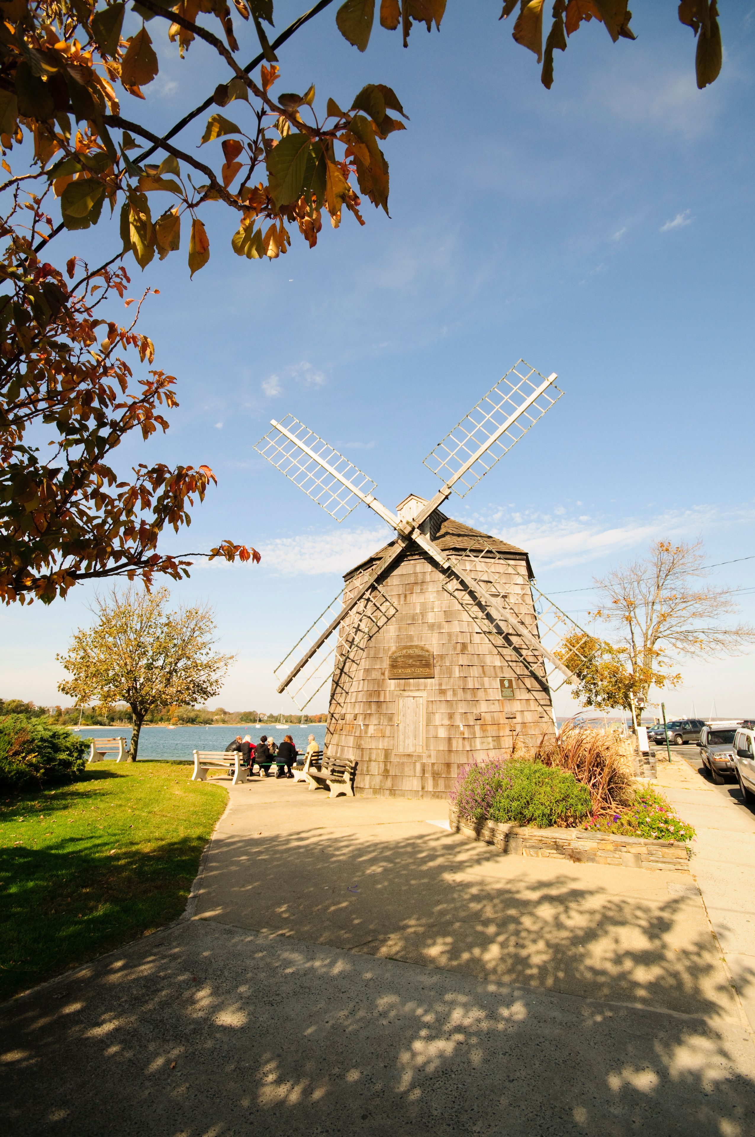 A traditional windmill with a wooden structure and a lattice roof, surrounded by a park with benches and a pathway.