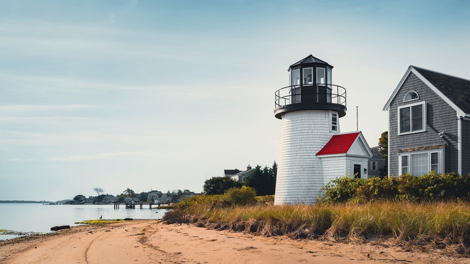 A lighthouse, a sandy beach, and a house with a red roof.