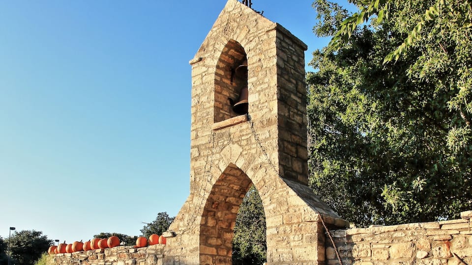 A stone archway with a cross atop, surrounded by pumpkins.
