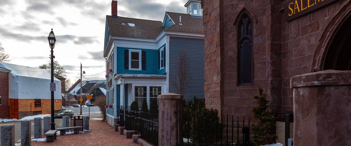 A brick-paved street with a blue house and a brick building with a sign reading "SALEM WIT".