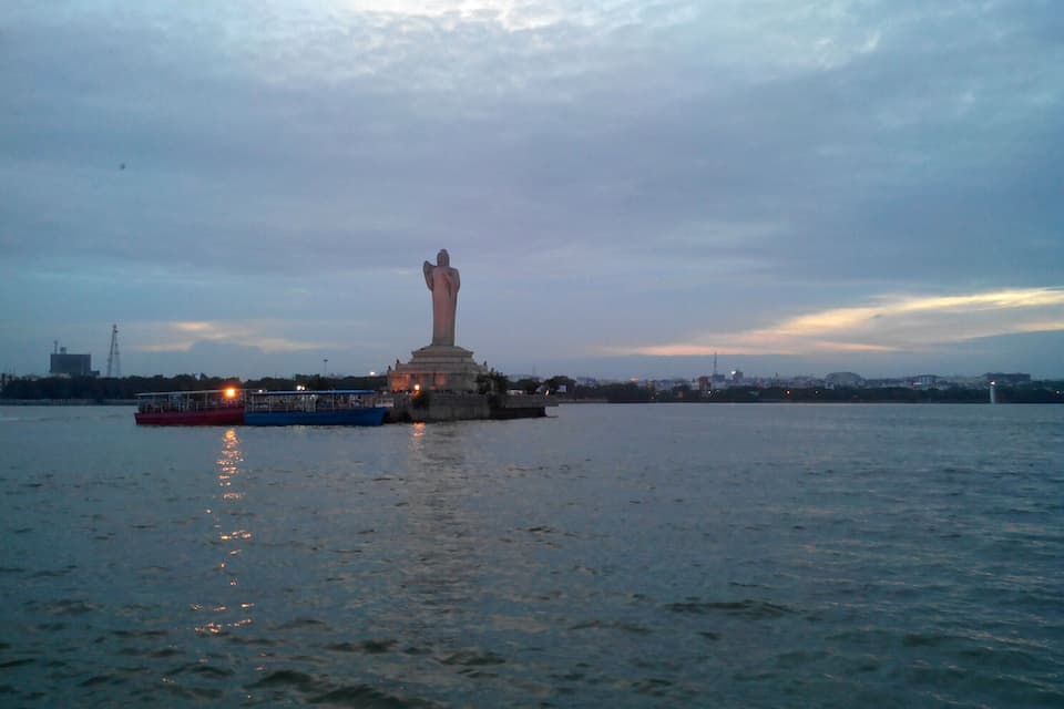 Eine große Statue auf einer künstlichen Insel inmitten von Wasser, im Vordergrund ein Boot.