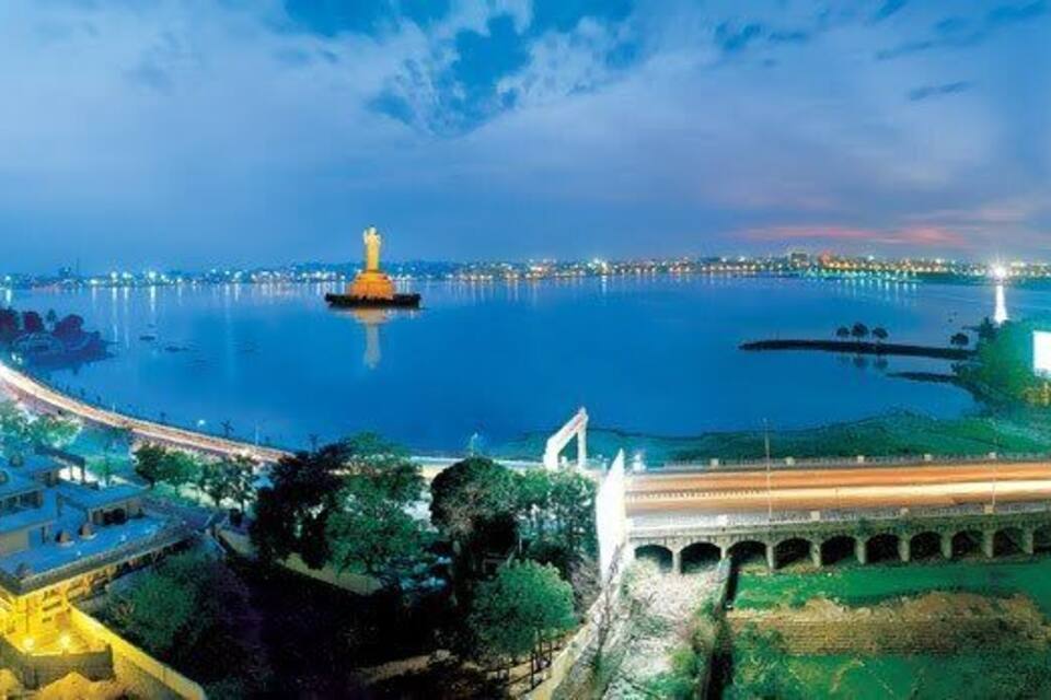 Paisagem urbana costeira noturna com um farol imponente, uma ponte e edifícios iluminados.