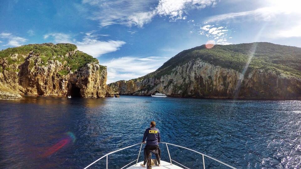 A boat on a calm sea with rocky cliffs and a clear sky.