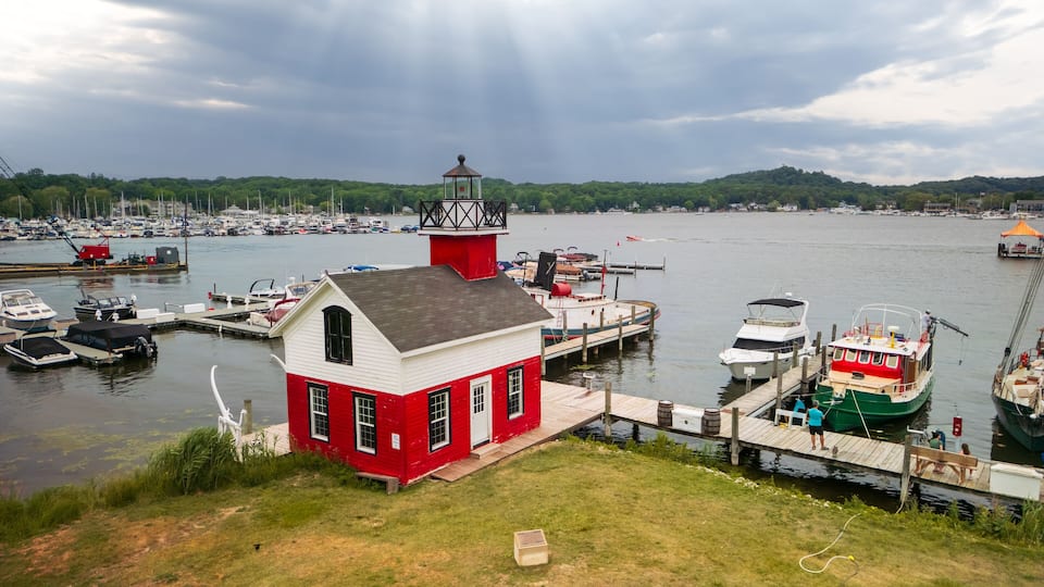A harbor with a red and white lighthouse, boats docked, and a green boat with a red cabin.