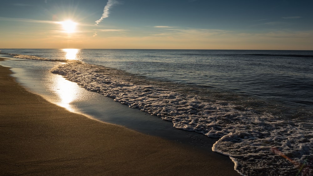 Une plage où la lumière du soleil se reflète sur l’eau et le sable.