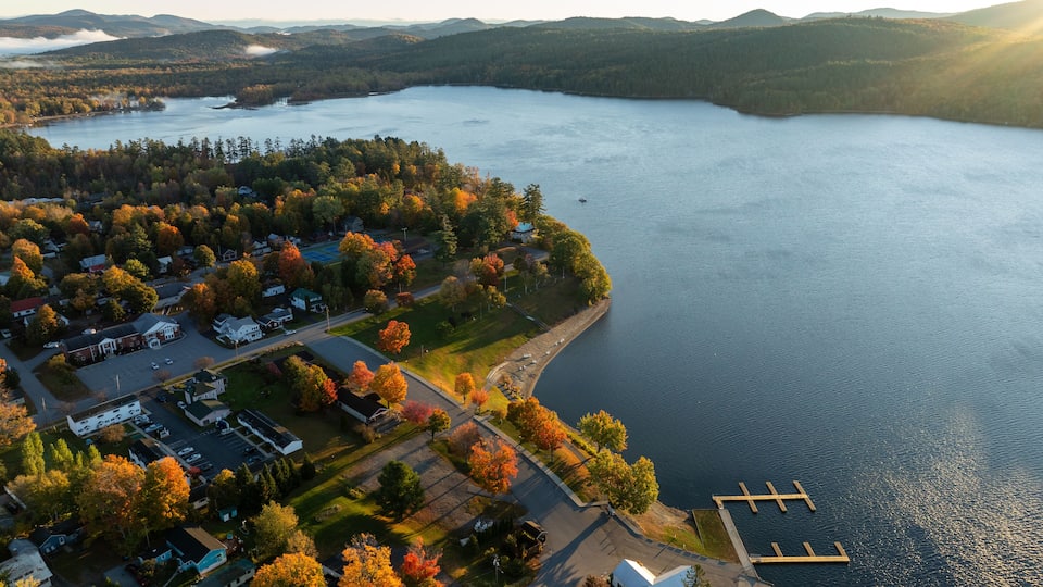 An aerial view of a lakeside community with houses, a dock, and autumn foliage.