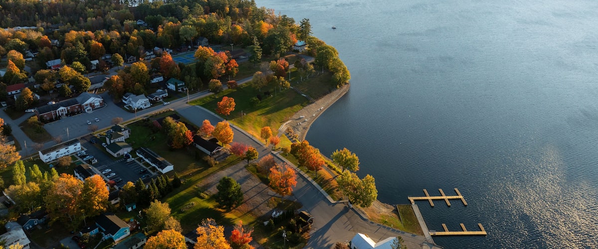 An aerial view of a lakeside community with houses, a dock, and autumn foliage.