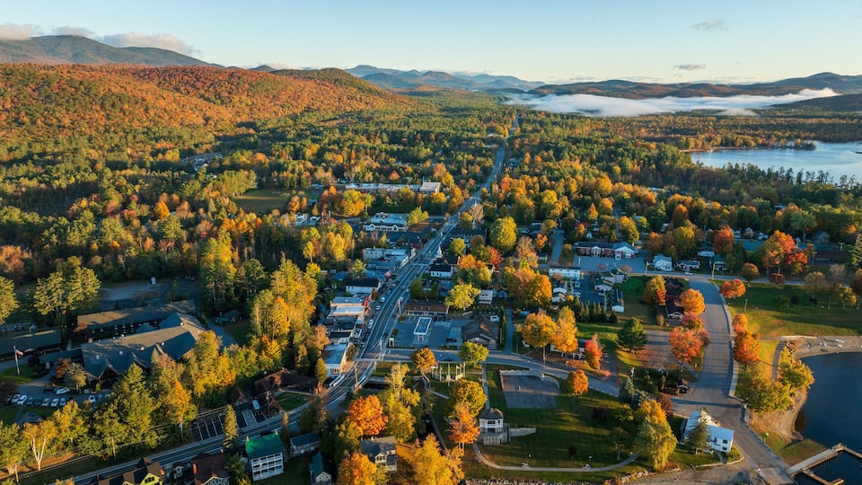 An aerial view of a town surrounded by autumn-colored forests and a lake.