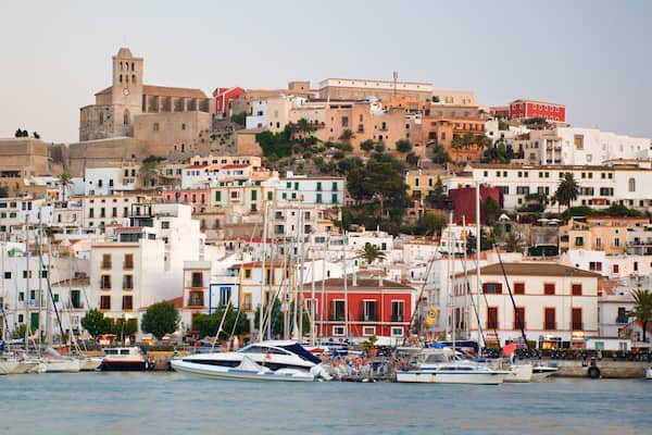 Una cittadina costiera con edifici storici, un'imponente torre e un porto turistico pieno di imbarcazioni.