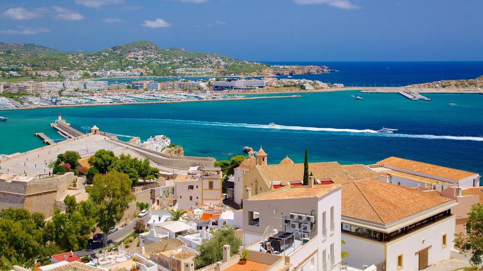 A coastal town with a marina, buildings, and a hilly landscape in the background.
