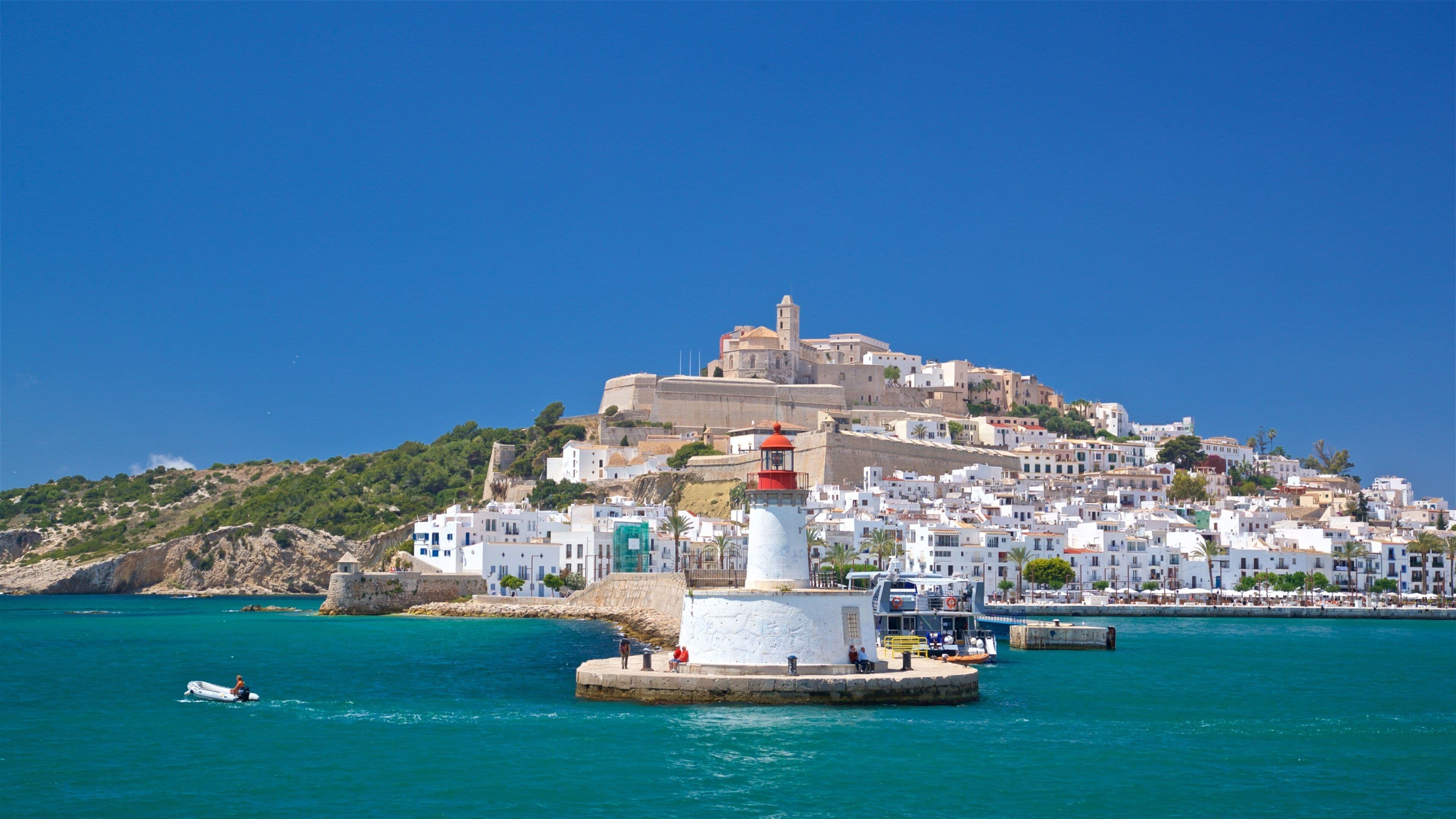 A coastal town with a prominent lighthouse, white buildings, and a historic fortress on a hill.