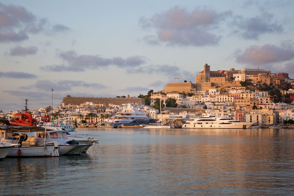 A coastal town with historic buildings, a prominent castle, and several yachts docked in the harbor.