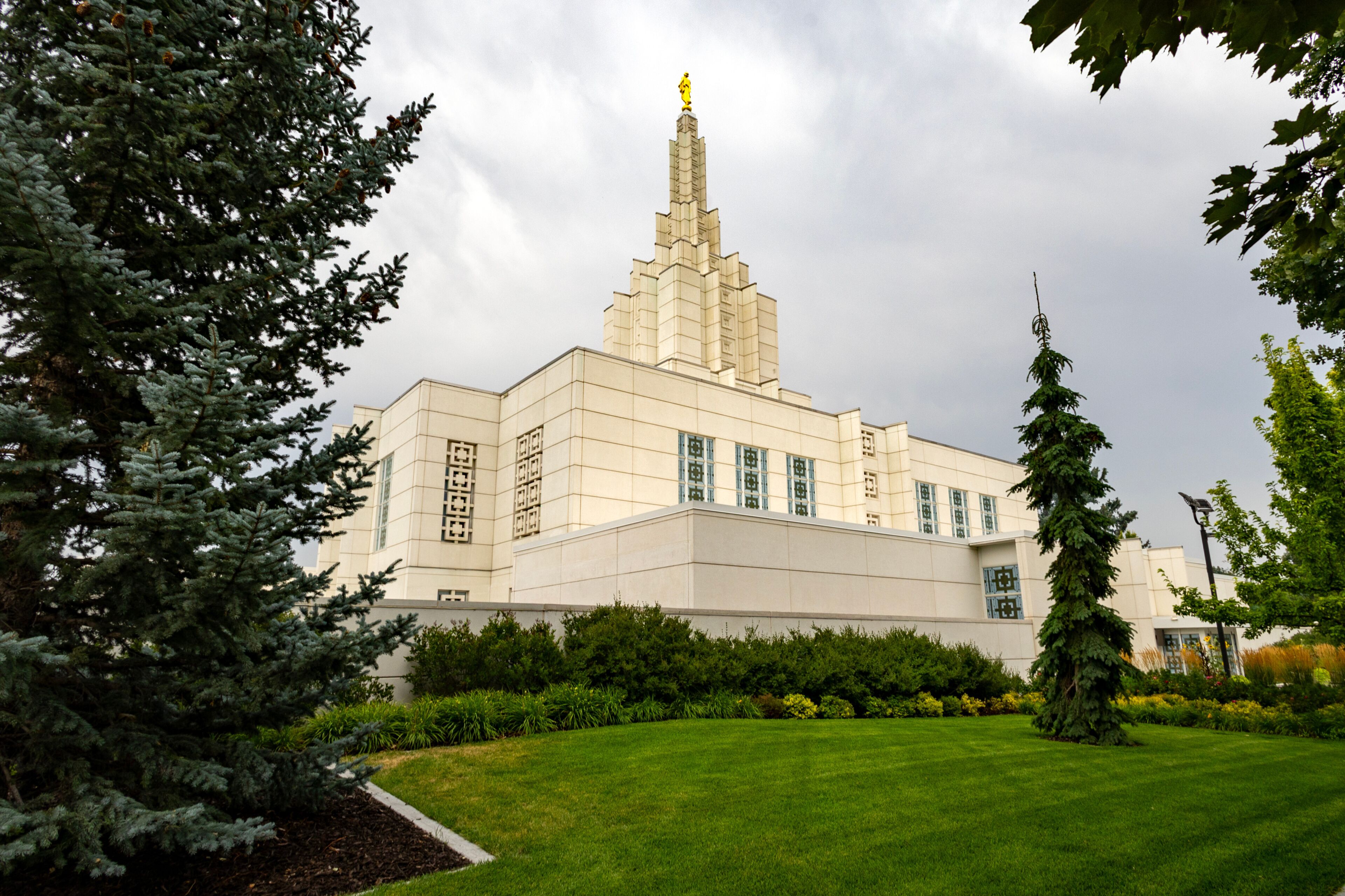 A large building with a tall spire and a statue on top, surrounded by greenery and trees.