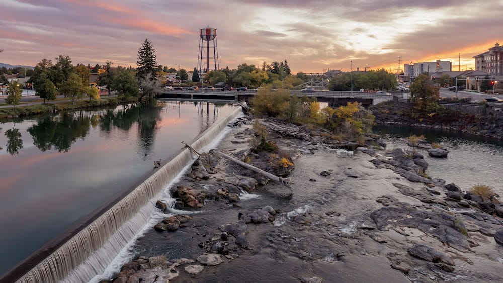 Peaceful river at sunset, with a small waterfall and geese. Town reflected in the water. Snake River, Idaho Falls, Idaho, USA.