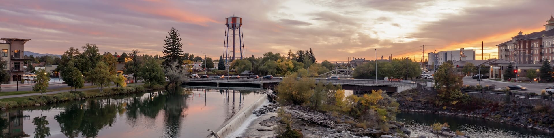 Peaceful river at sunset, with a small waterfall and geese. Town reflected in the water. Snake River, Idaho Falls, Idaho, USA.