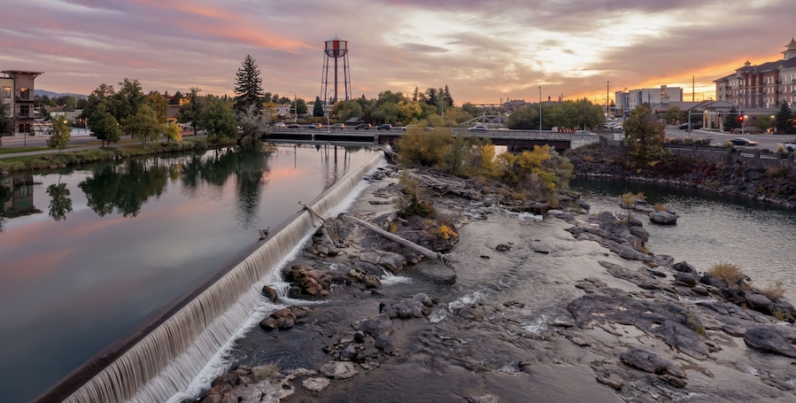 Peaceful river at sunset, with a small waterfall and geese. Town reflected in the water. Snake River, Idaho Falls, Idaho, USA.
