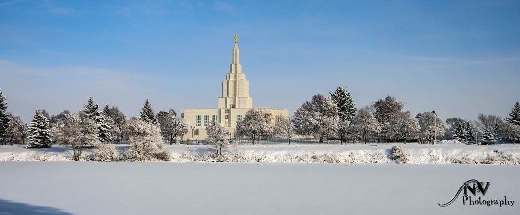 A snow-covered landscape with a prominent building featuring a tall spire, surrounded by trees.