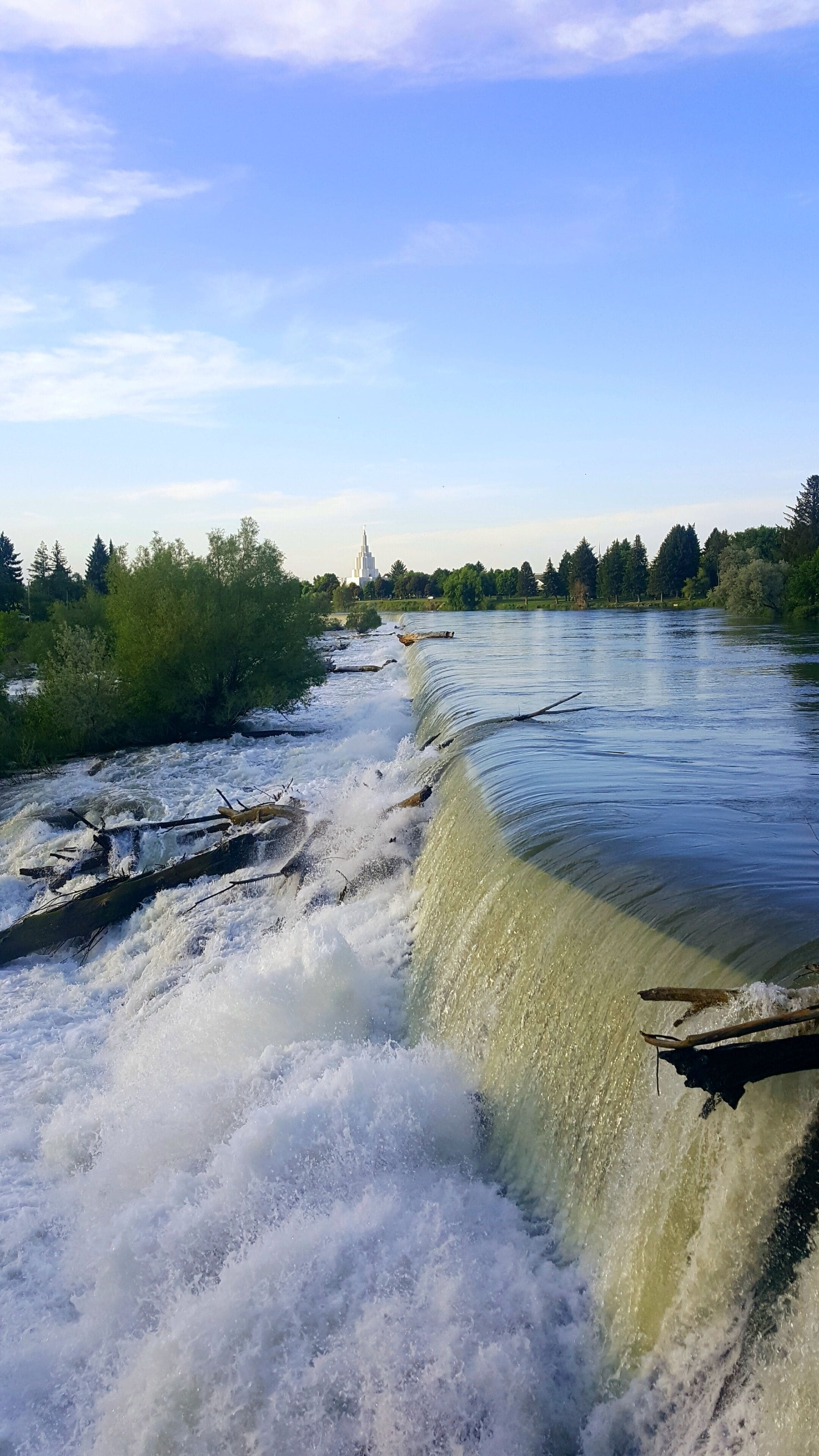A river with a dam, trees, and a distant tower.