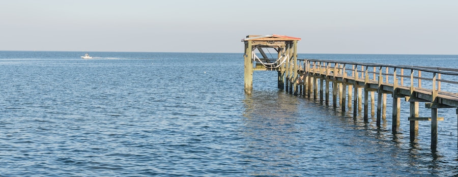 Fishing piers stretching out over Galveston Bay in Kemah, Texas, USA. Foot pier for saltwater fishing of vacation home/beach house rental/bay home in Lighthouse District waterfront at sunset. Panorama
