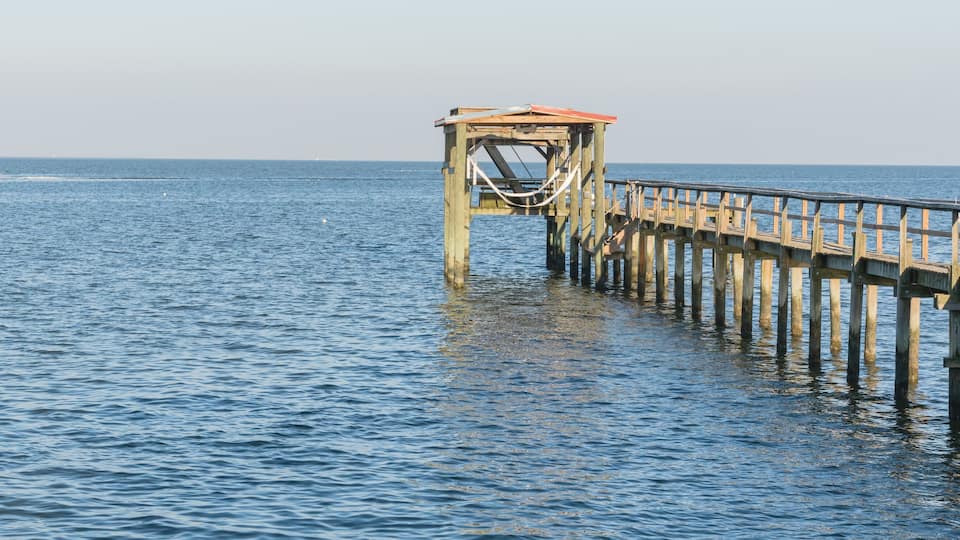 A wooden pier extending into calm blue waters with a small boat in the distance.
