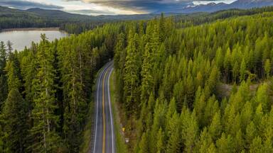 High angle view of a winding road through a lush forest, leading to a lake. Scenic mountain range in the background. , Seeley Lake, Montana, USA.