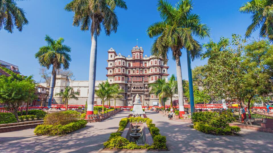 A historic building with a central fountain, surrounded by palm trees and well-maintained gardens.