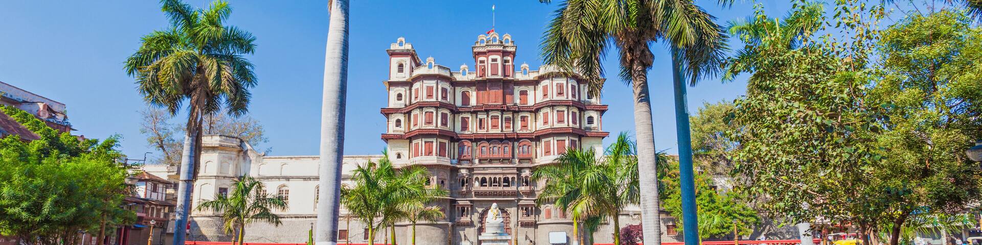 A historic building with a central fountain, surrounded by palm trees and well-maintained gardens.