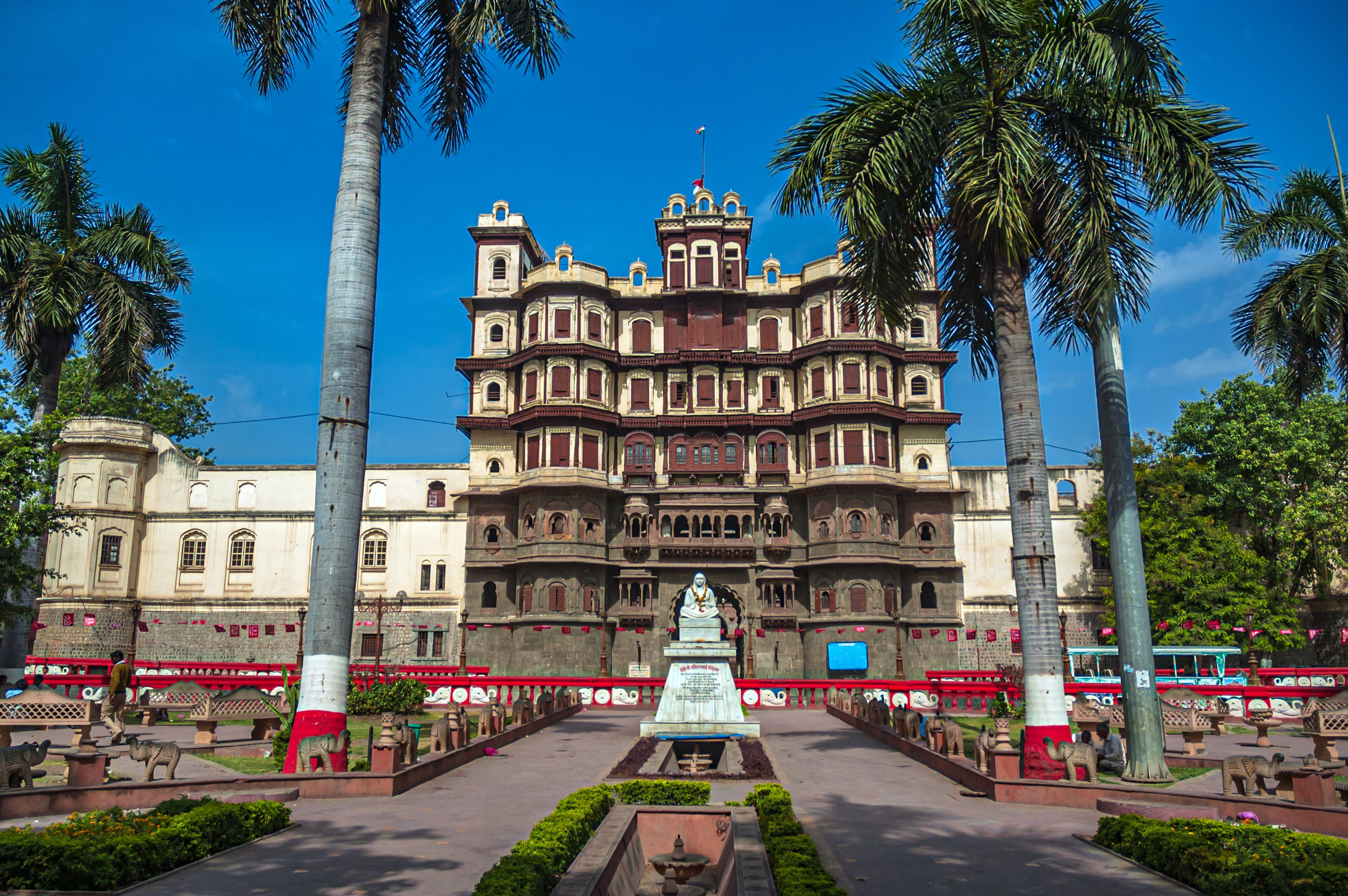 A historic building with ornate architecture, palm trees, and a central statue.