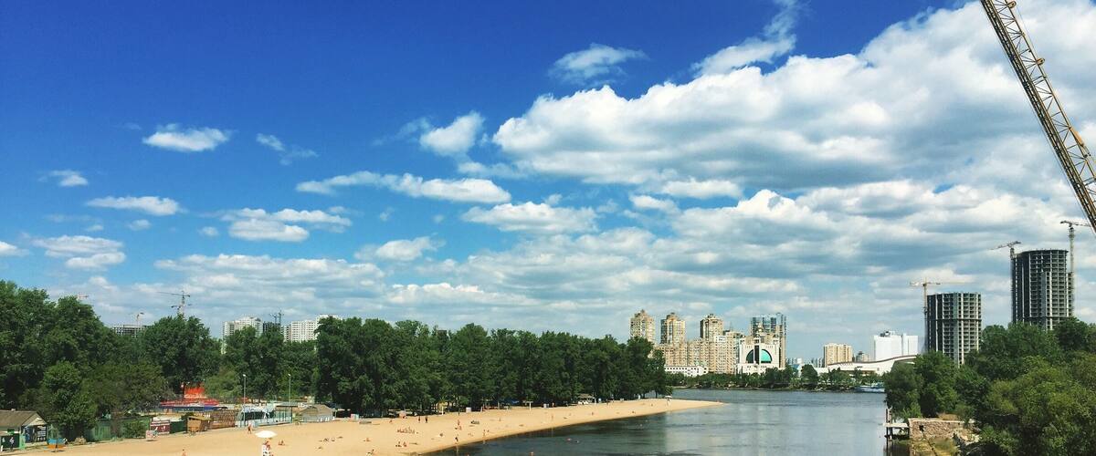 A river with a sandy beach, trees, and buildings in the background.