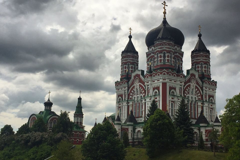 A large, ornate church with multiple domes and crosses, surrounded by lush greenery.