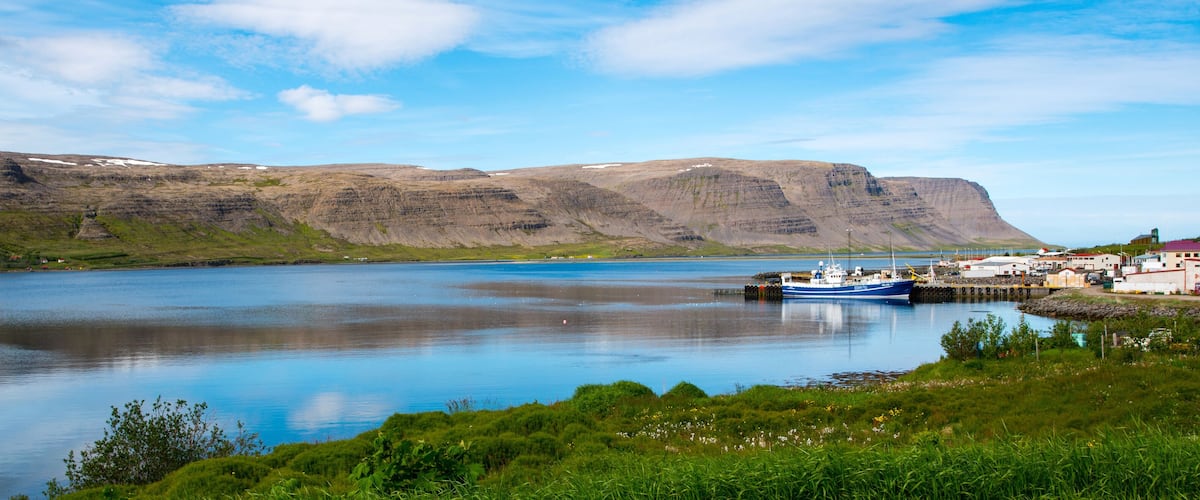 A calm lake with a boat docked at a pier, surrounded by green hills and a clear sky.