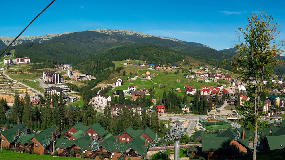 A mountainous town with ski lifts, houses, and a winding road.
