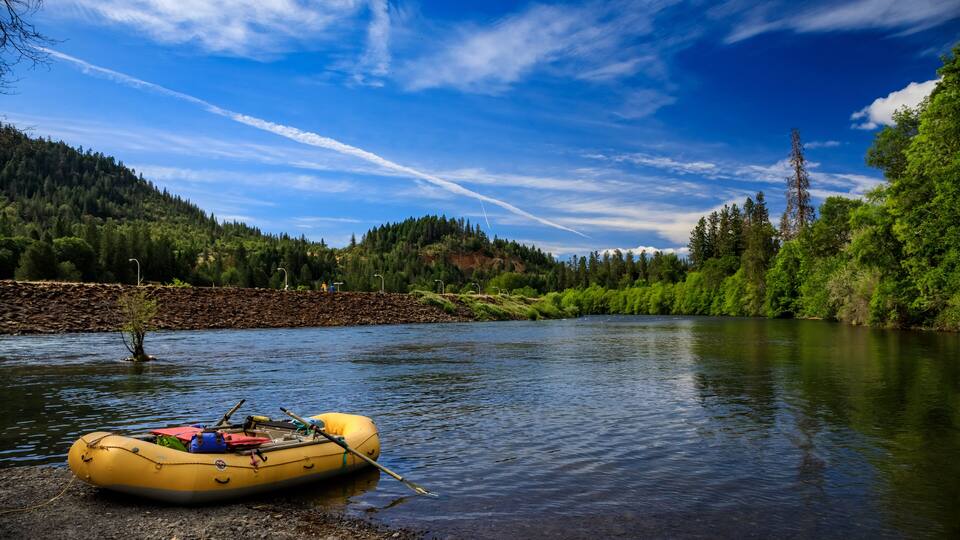 A yellow raft on a calm river, surrounded by lush greenery and a clear blue sky.
