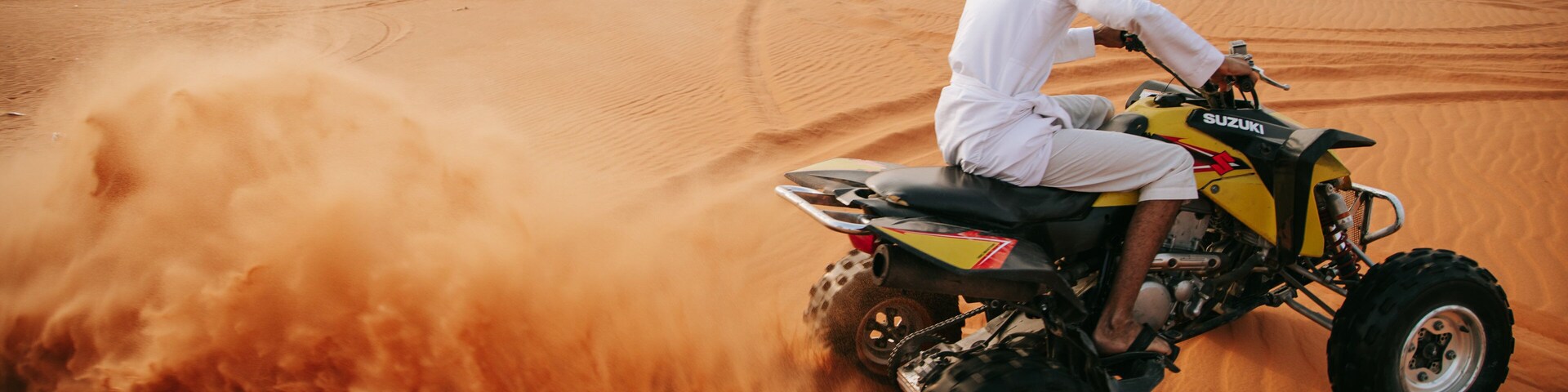 A person riding a yellow ATV in a desert with sand dunes.
