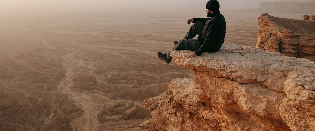 A person sitting on a rock ledge overlooking a vast desert landscape.