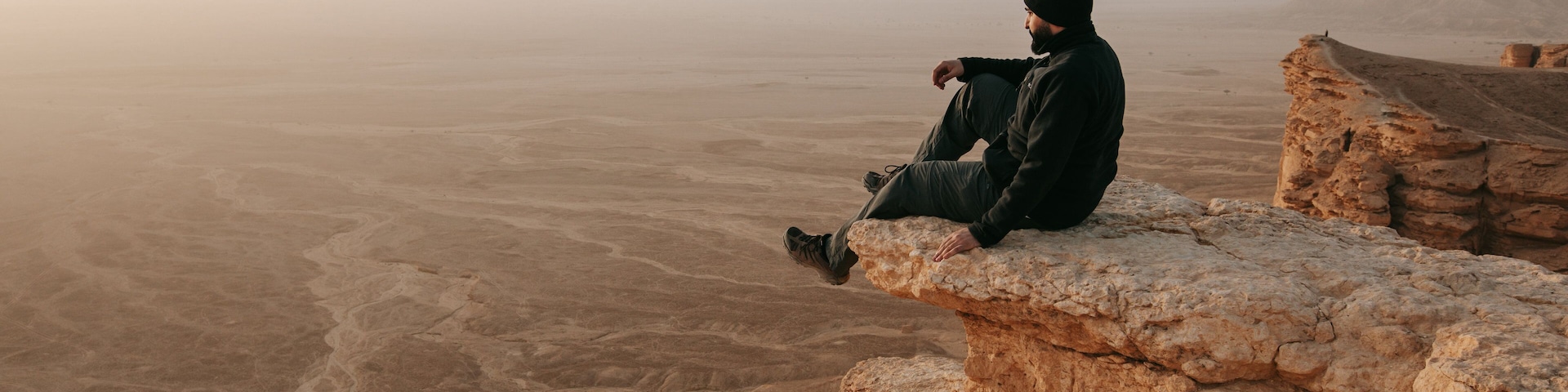 A person sitting on a rock ledge overlooking a vast desert landscape.