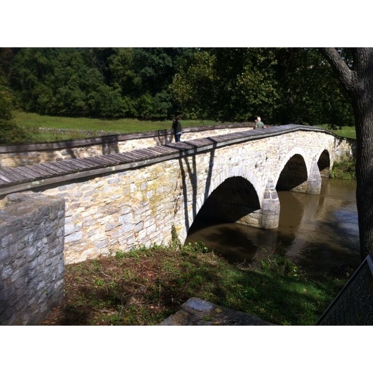 A stone bridge with three arches over a river, surrounded by greenery.