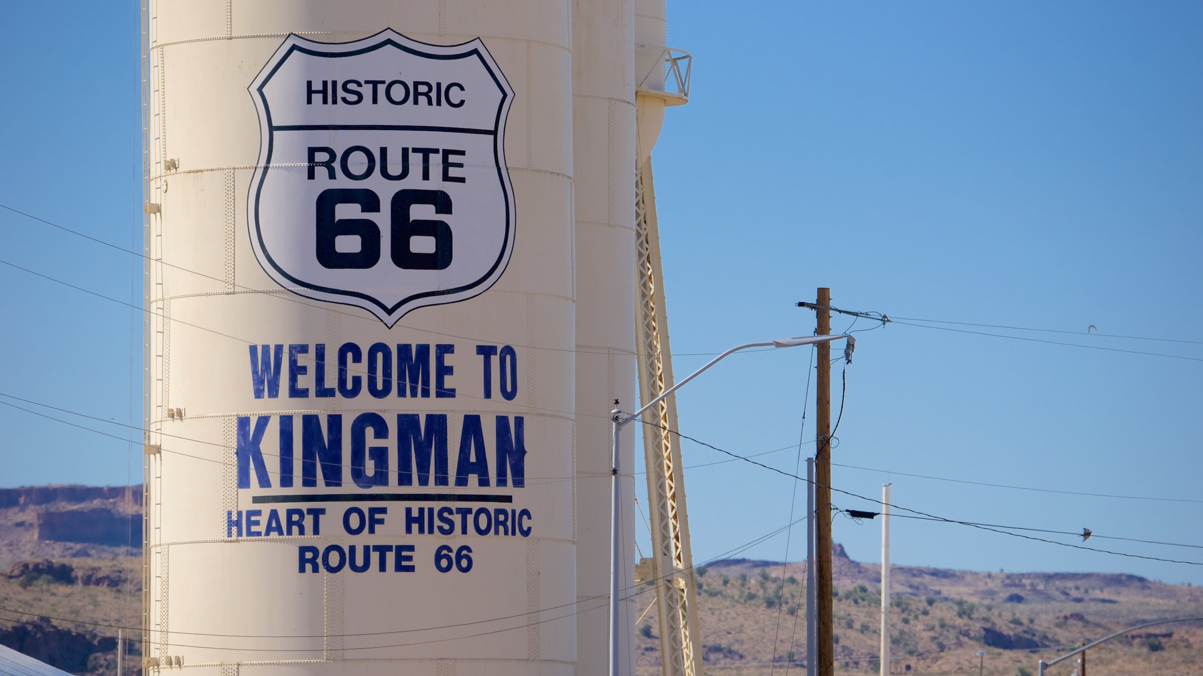 A large white sign with blue lettering that reads "Historic Route 66 Welcome to Kingman Heart of Historic Route 66."