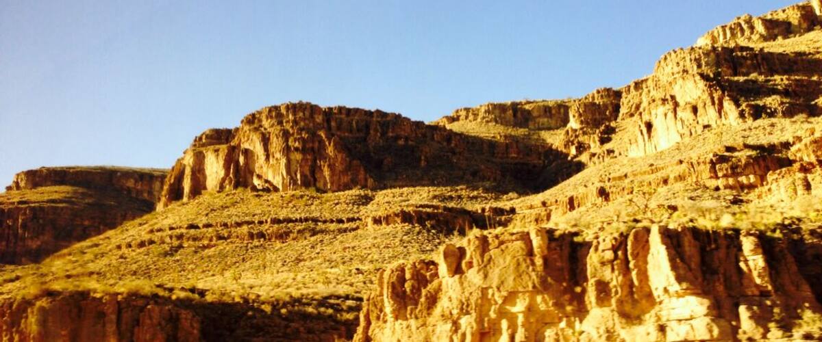 A canyon with layered rock formations and sparse vegetation.